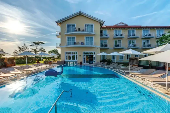 Outdoor swimming pool with sun loungers and a building in the background.