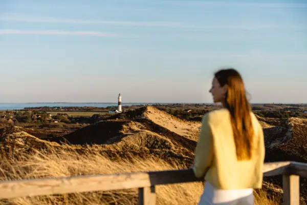 A woman is standing on the Uwe Düne on Sylt, looking at a lighthouse.