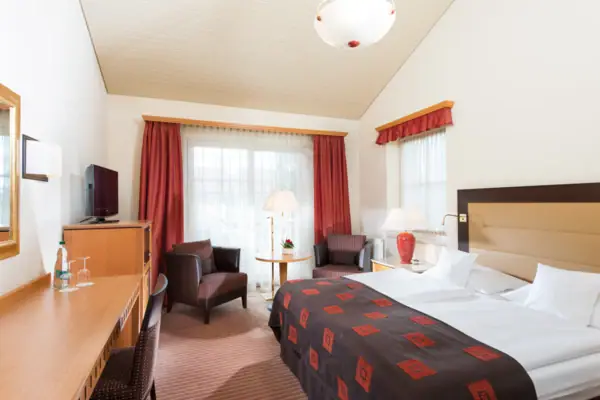 A room with a neatly made bed and two chairs.