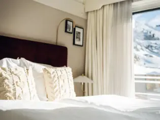 Cozy hotel room featuring a bed with plush pillows and a window in the background.