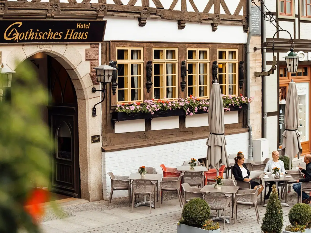 Hotelfassade Eine Gruppe von Menschen sitzt an Tischen im Freien vor einem Gebäude.