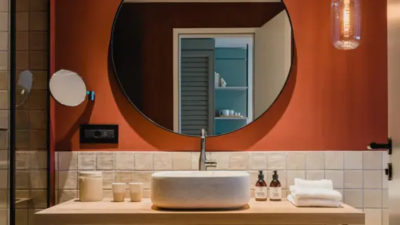 Modern bathroom featuring a round mirror above a sink with a visible tap and tiled countertop.