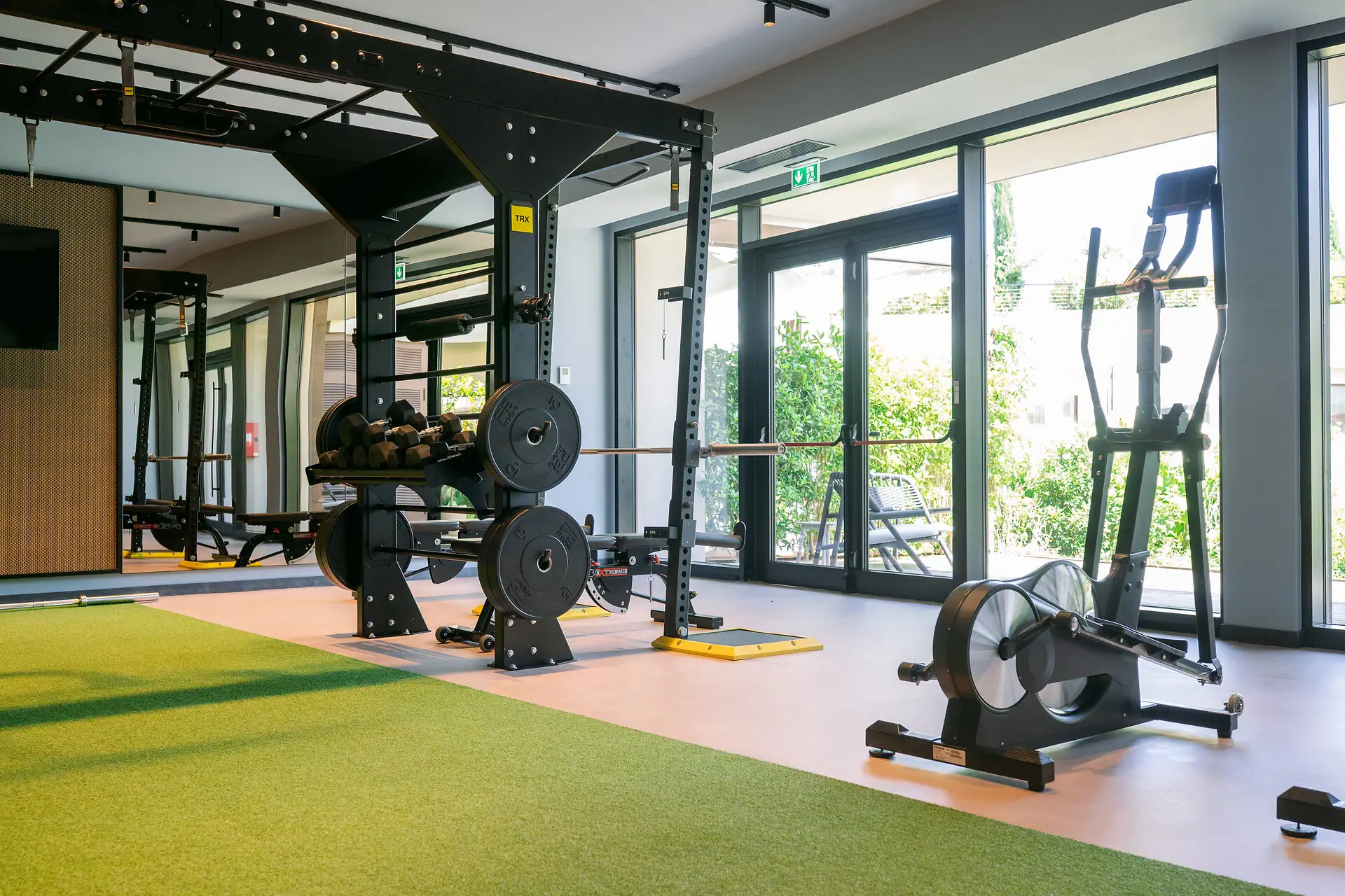 Cardio-Bereich im Fitnessstudio Cardio-Geräte wie Ergometer im Fitnessraum des A-ROSA Gardasee mit Blick ins Grüne.