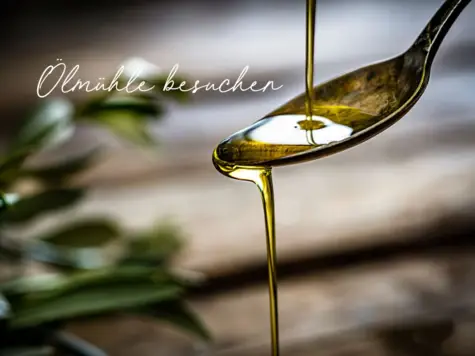 A spoon on which olive oil is flowing and a wooden table with olive leaves can be seen in the background.