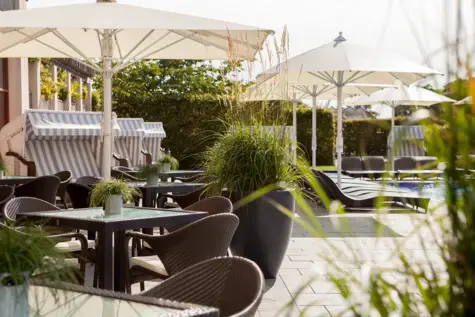 Outdoor seating area with chairs, tables, umbrellas, and decorative plants.