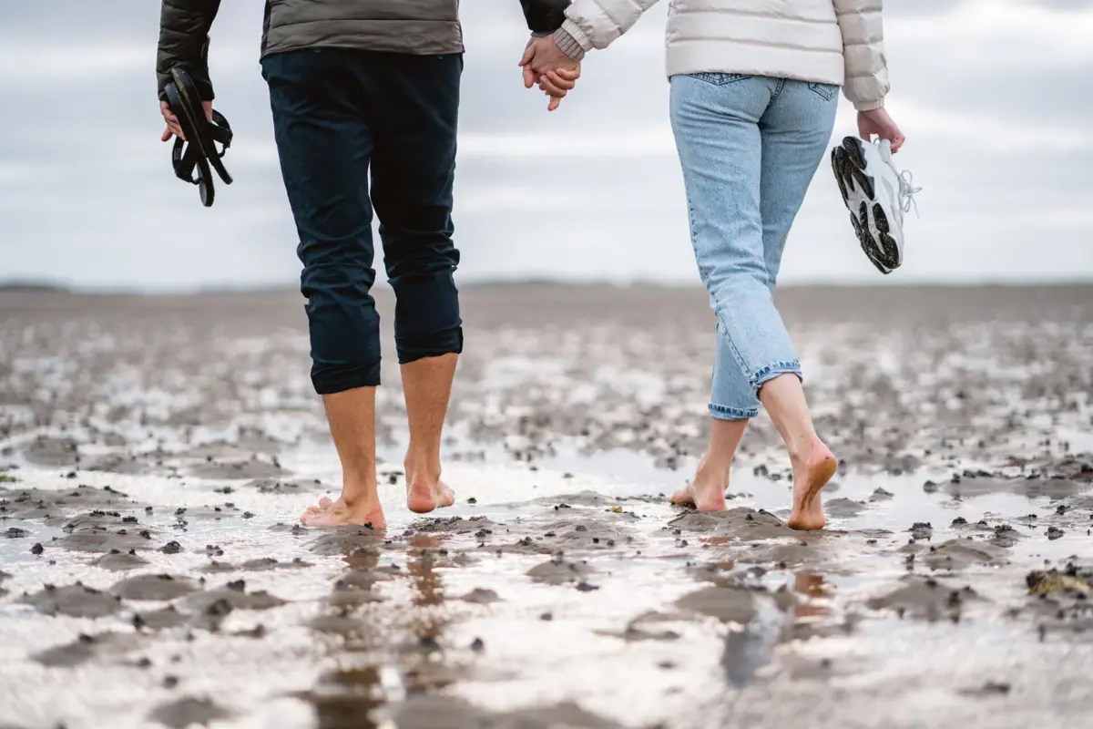 A man and a woman are holding hands and going for a walk on the mudflats on Sylt.