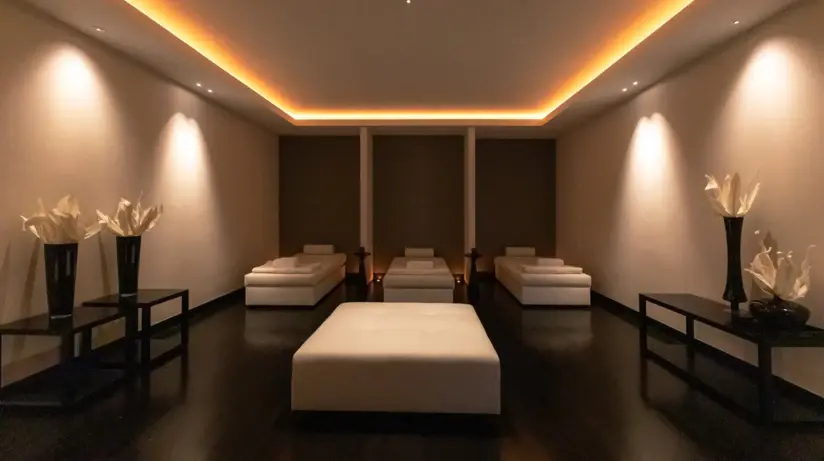 A relaxation room in pleasant light with white lounge beds and small black tables with flower vases on the walls.