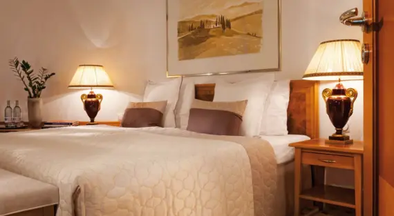 A bed with pillows, bed linen and bedside lamps, plus a painting on the wall.