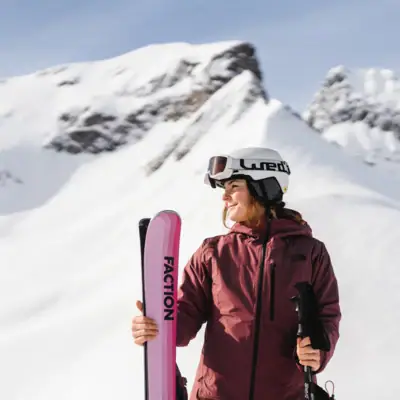 A woman with skis and poles in front of snow-capped mountains
