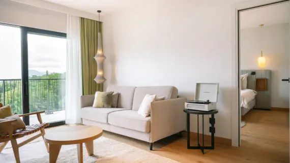 Living area of a suite with couch and coffee table and a passageway to the bedroom behind.