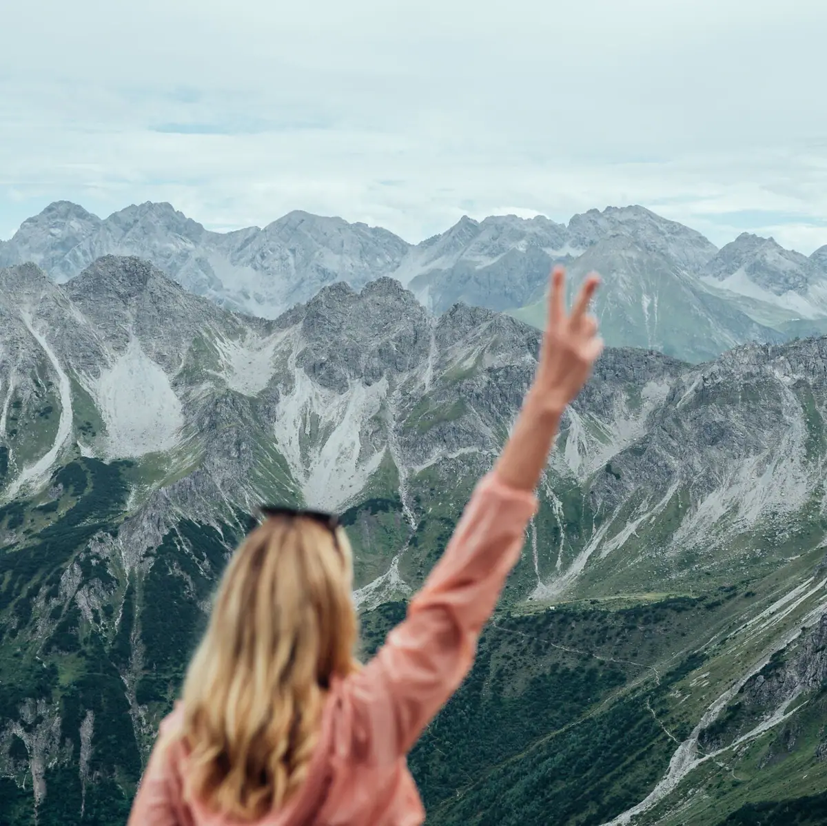 A woman stands on a mountain with her hand raised.
