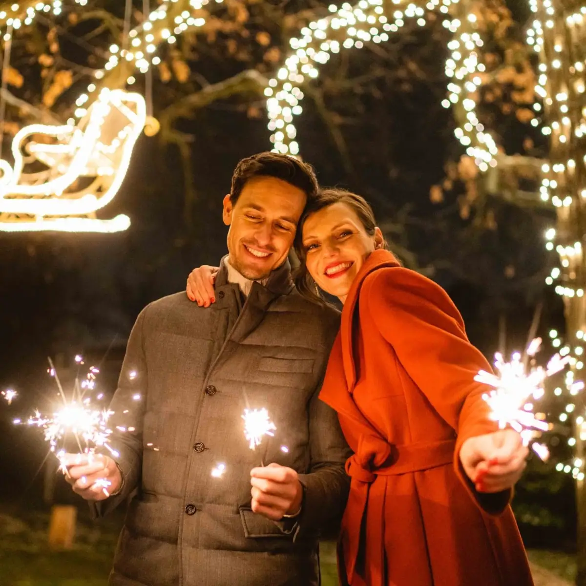 A man and a woman hold sparklers in front of fairy lights.