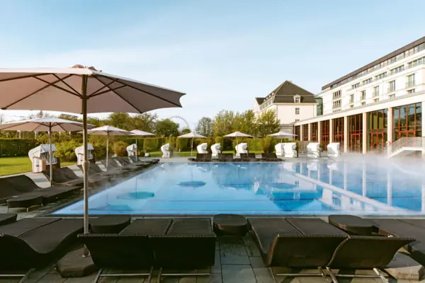 Large white building with pool and trees in the foreground.