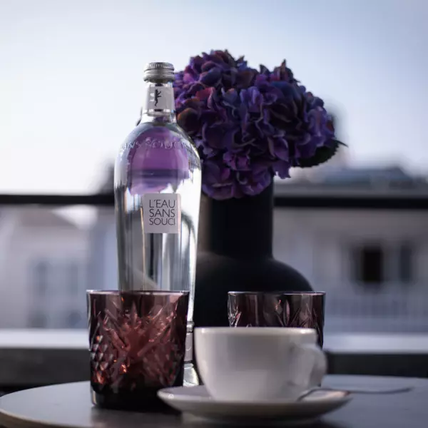 A bottle of water, purple tea lights and a cup of coffee on a table on a balcony.