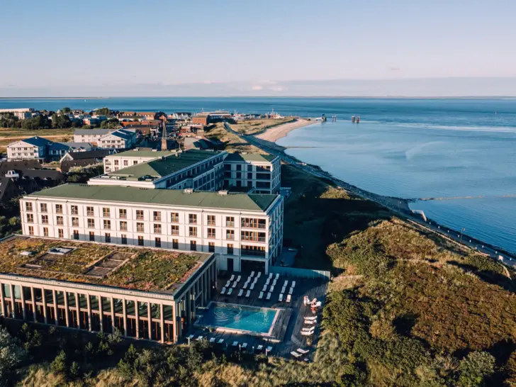 Aerial view of a building with a pool and a beach leading into the sea in the background.