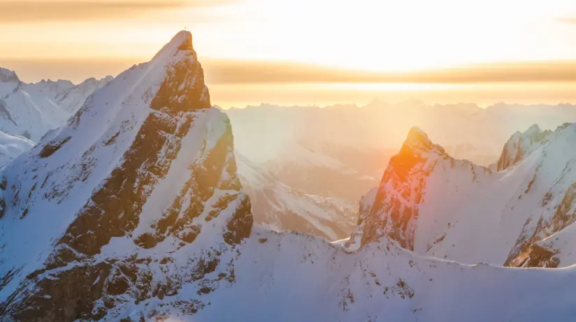 Snowy mountain peaks with sunlight piercing through clouds.