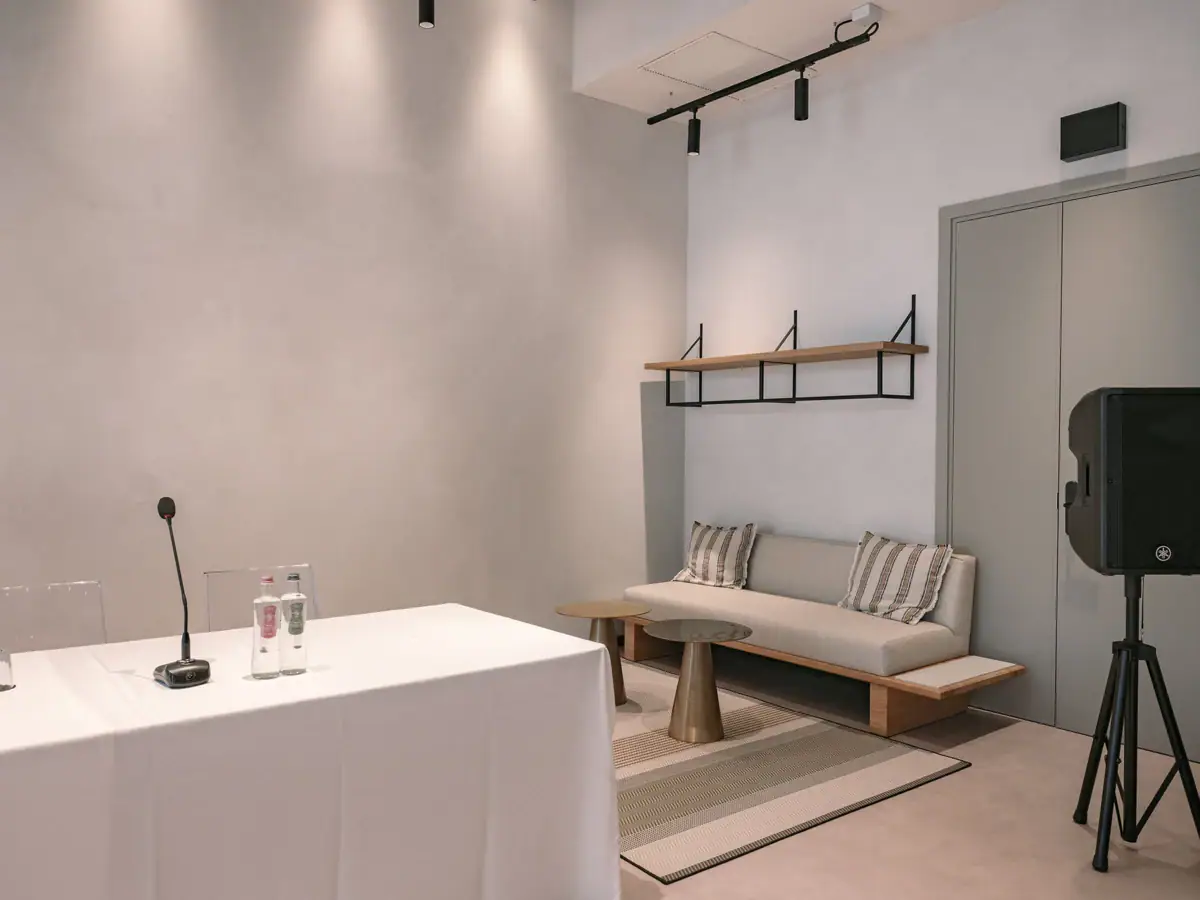 Creavista im A-ROSA Gardasee Ein Tagungsraum mit einem weißen Tisch und einer Couch. Auf dem Tisch steht ein Mikrofon, neben dem Tisch steht ein Lautsprecher.