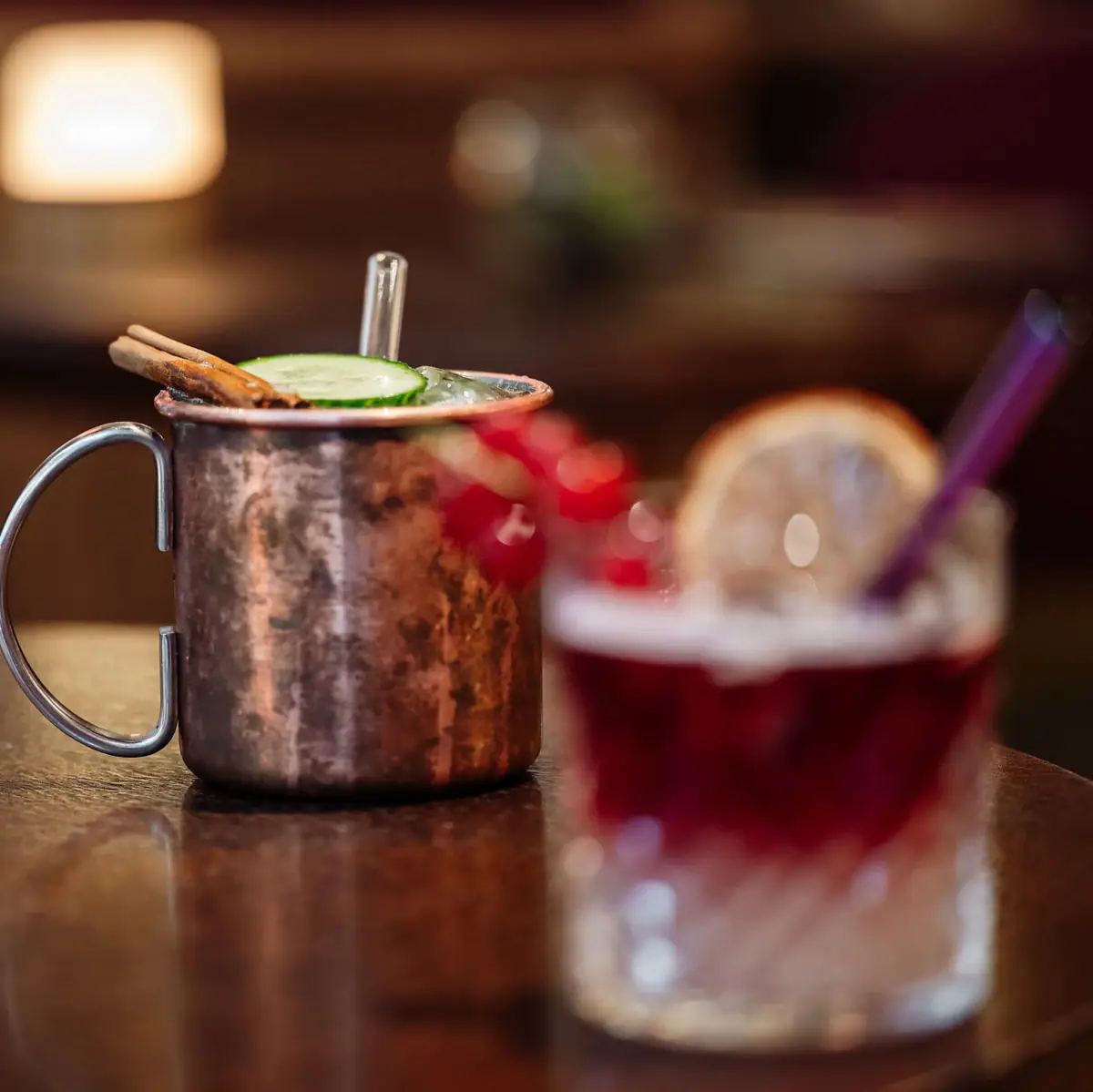 A copper mug with a slice of cucumber and a straw on a table