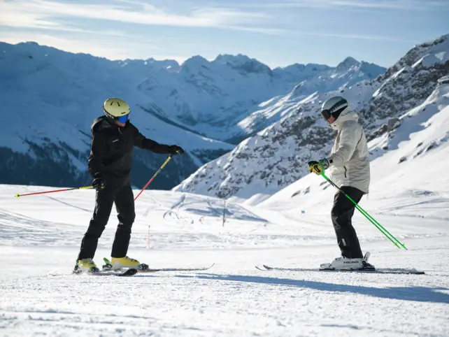 Group of skiers gliding down a snowy slope with snowy mountains in the back.