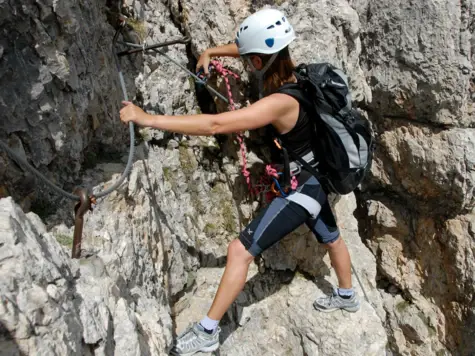 Woman climbing on a rock face, equipped with climbing harness and helmet.