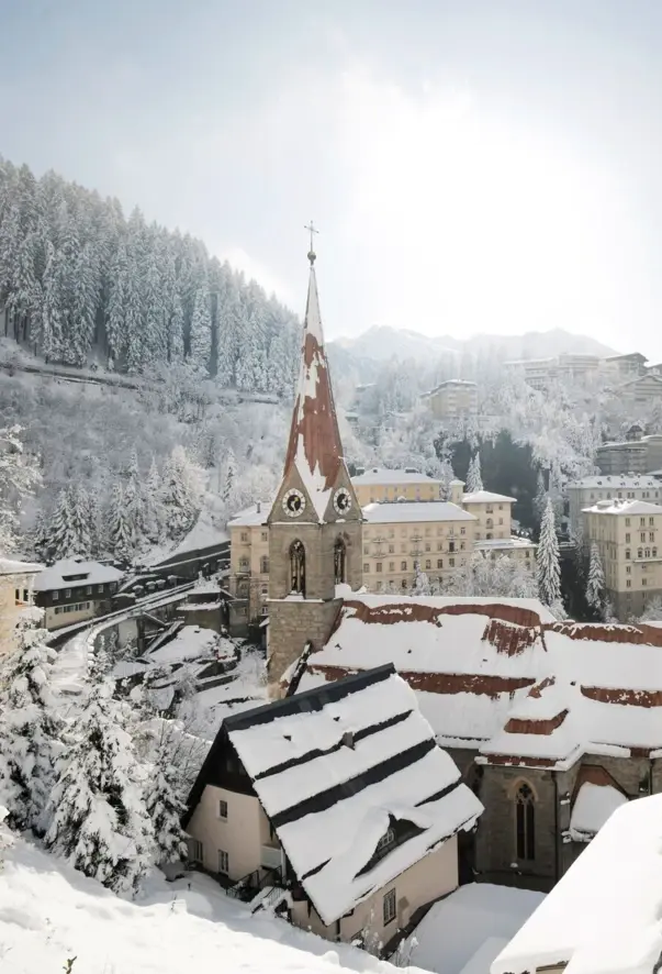 Snow-covered town with houses, a church and a mountain in the background on a clear winter's day.