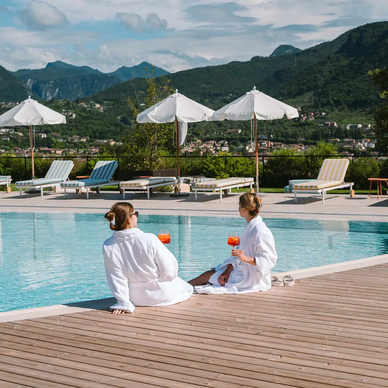 Zwei Frauen sitzen mit einem Aperil in der Hand am Pool. 