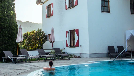 A woman ist swimming in an outdoor pool infant of a white building looking into the distance. 