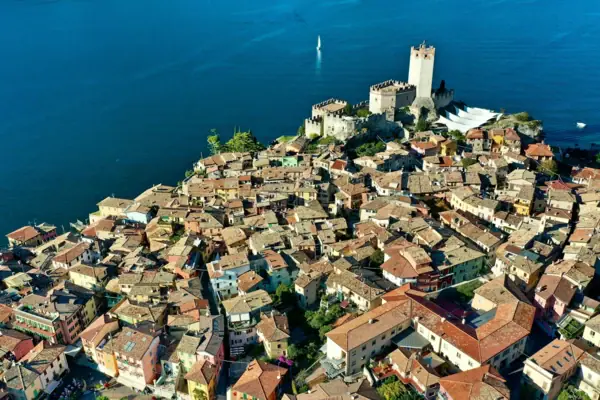 Malcesine An aerial view of a town with a castle on the outskirts, surrounded by water.