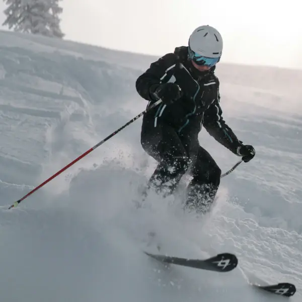 Person skiing down a snowy slope with ski poles in hand.