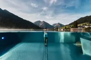 A person stands in a pool with mountains in the background.