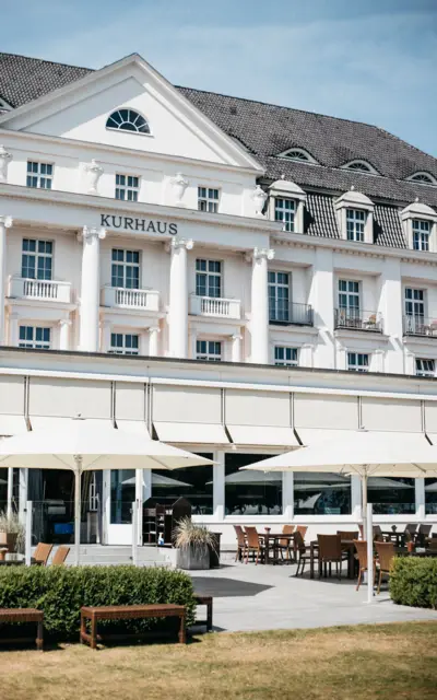 A white building with columns, featuring outdoor seating with tables and chairs.