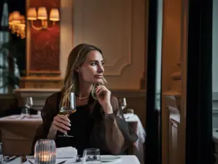 A woman holds a wine glass in her hand in an interior room.