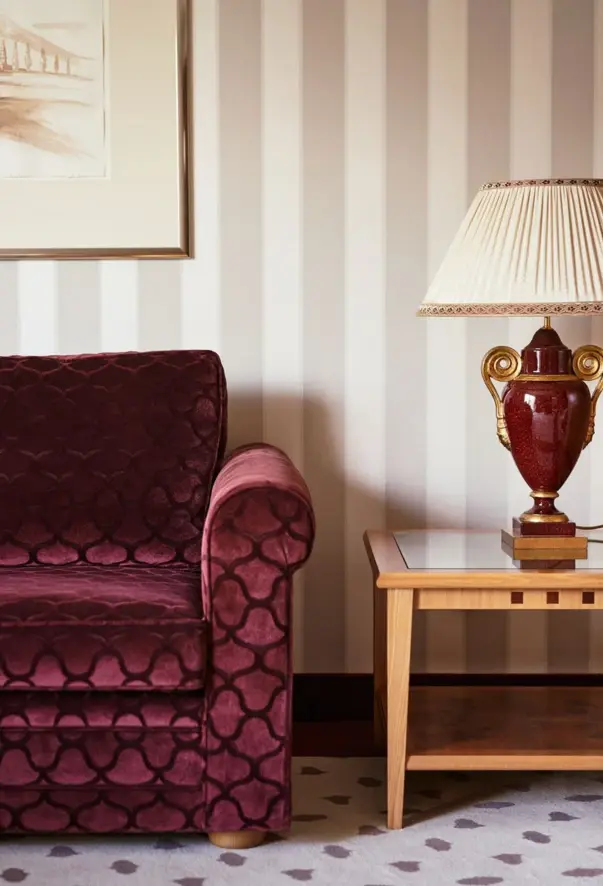 Bordeaux red sofa in front of beige striped wallpaper next to a lamp on a side table.