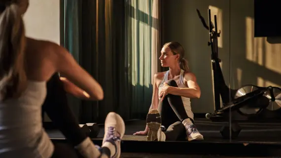 Woman sitting on the floor in a fitness room and stretching her legs.