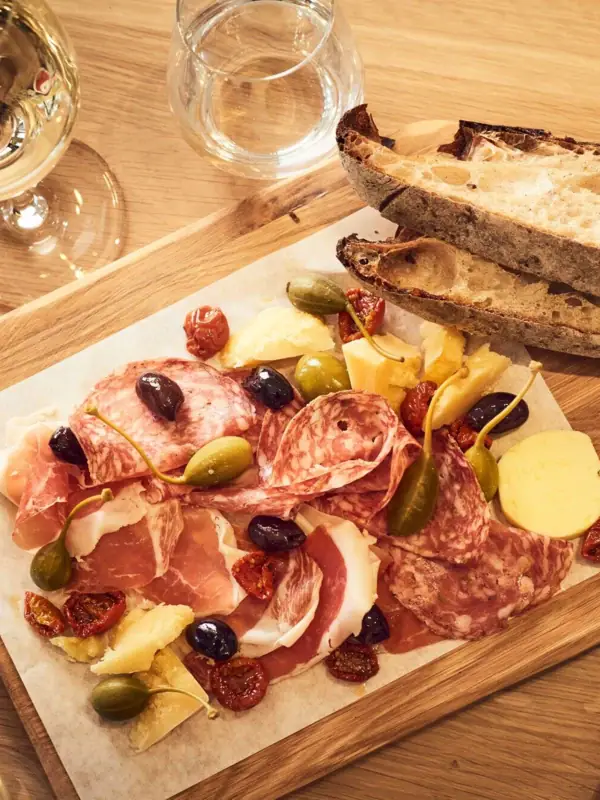 A plate of assorted meats and cheeses with bread, accompanied by wine glasses.