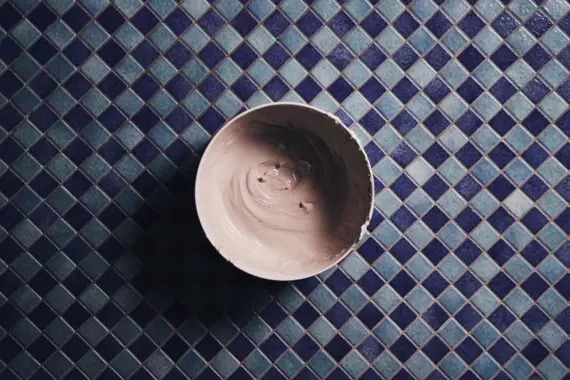 A bowl with a clay mask stands on small blue tiles. 