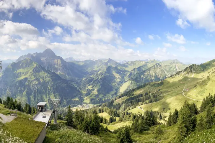Mountain landscape with buildings and trees under a blue sky with some clouds.