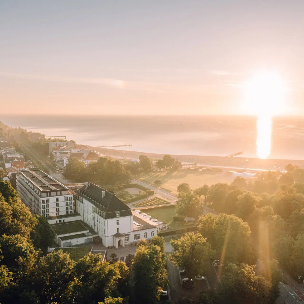 Ein großes Hotelgebäude umgeben von Bäumen vor einer Küste bei Sonnenaufgang.