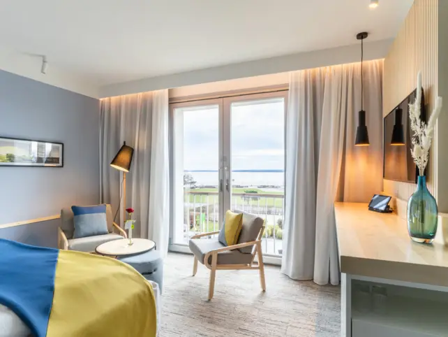 Interior view of a hotel room with a bed, table and chairs.