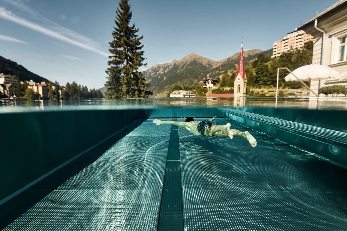 Guest swimming in the infinity pool with panoramic mountain views at the Straubinger Grand Hotel in Bad Gastein.