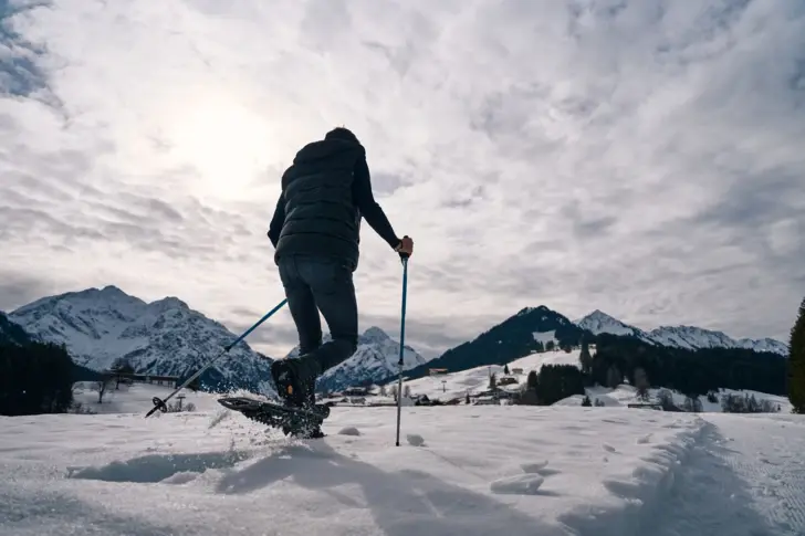 Person with snowshoes and poles on a snowy landscape.
