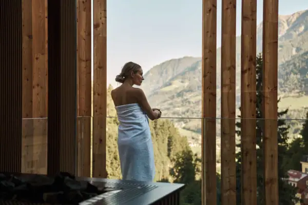 A woman in a white towel standing in front of a window overlooking a valley.