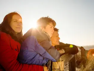 A family is leaning against a fence, smiling and wearing winter clothes.