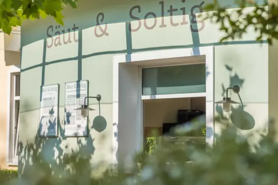 Building labeled "Säut & Soltig" with a kiosk sales hatch and menus on the wall, surrounded by plants.