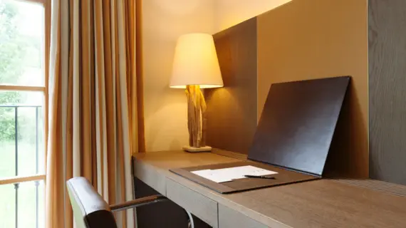 A dark wood desk with a folder containing a pad and a pen. A lamp can be seen in the far corner. 