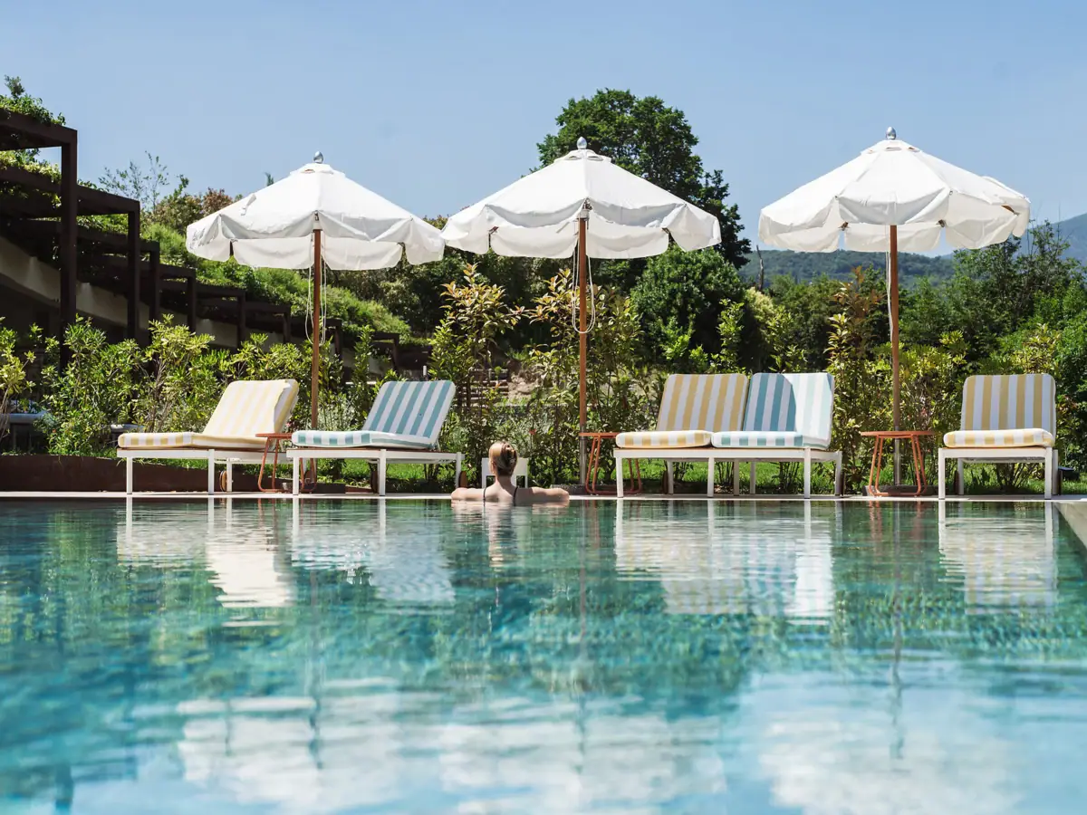 Eine Person im Pool mit Sonnenschirmen und Liegestühlen.