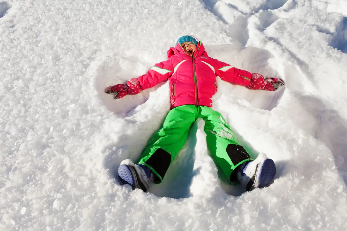 A child is lying in the snow, making a snow angel.