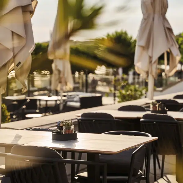 Outdoor seating area with tables, chairs, and umbrellas surrounded by trees.