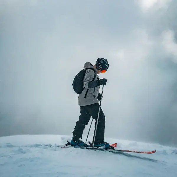 A man in ski equipment stands on skis and carries a rucksack on his back. 