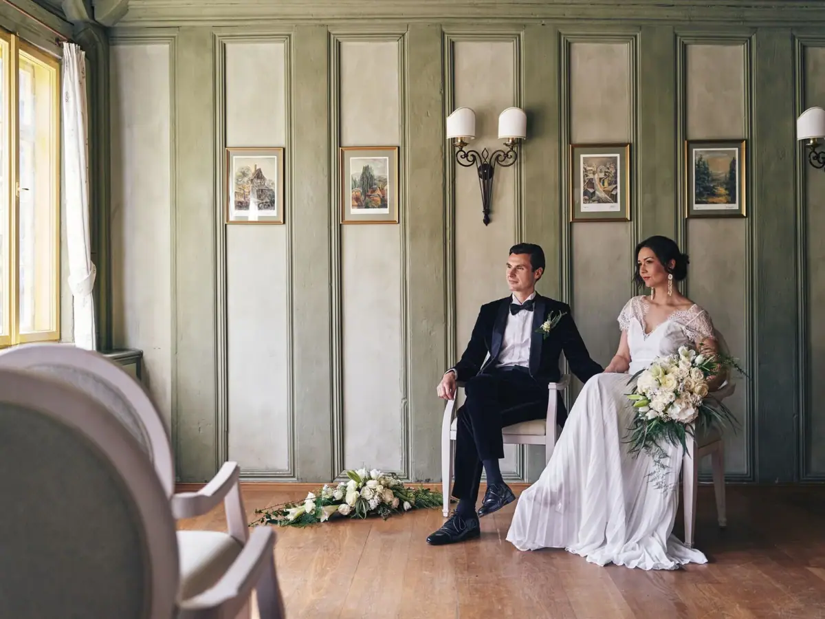 Ein Mann und eine Frau in Hochzeitskleidung sitzen auf Stühlen.